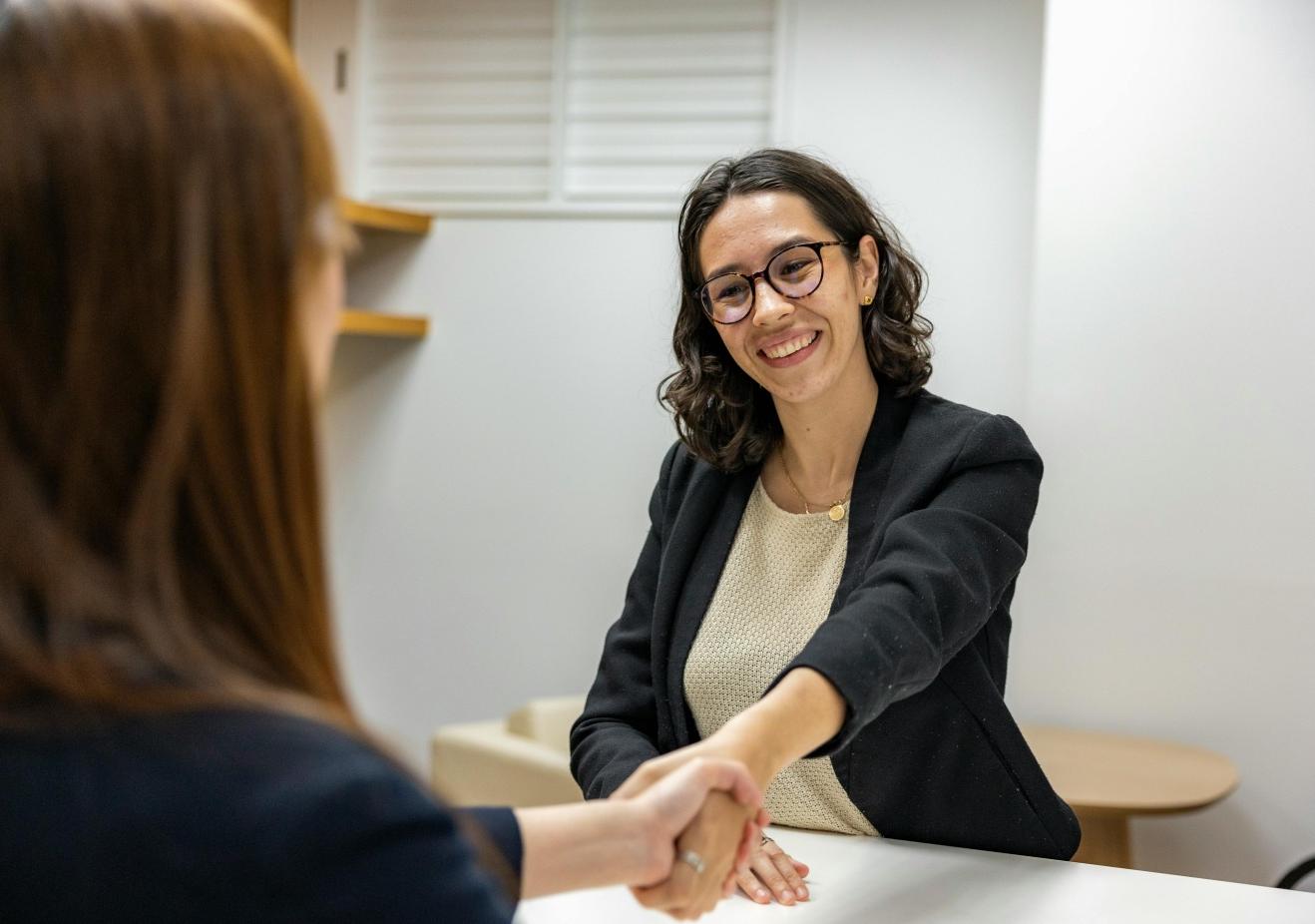 Two people shaking hands while sitting across from one another at a table.